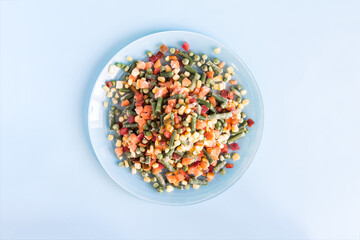 A mixture of frozen vegetables in a light plate on a light background. The concept of using quick-frozen products
