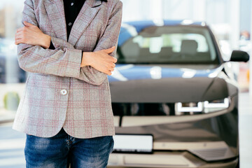 Close up of woman inside car dealership while standing in front of shiny new model of car or electric car.