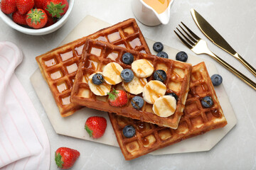 Fototapeta na wymiar Delicious Belgian waffles with banana, berries and caramel sauce on light marble table, flat lay