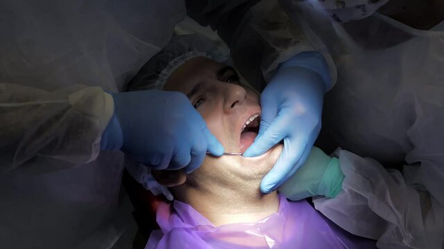 The dentist and his assistant treat the patient. Dental treatment in modern dentistry. A close-up shot of a patient in a dental chair undergoing a tooth extraction procedure. Medicine and healthcare.