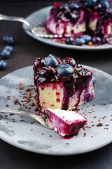 Traditioneller Heidelbeeren Käsekuchen mit frischen Beeren, Kompott und Schokoladenstreuseln serviert als close-up auf einem Design Teller 