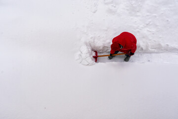A woman in a red jacket is digging a path through a thick layer of fresh snow. Winter landscape....