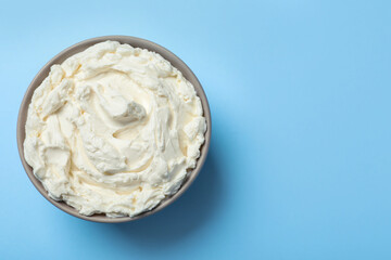 Bowl of tasty cream cheese on light blue background, top view. Space for text