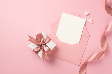 Top view photo of white giftbox with pink bow small hearts curly silk ribbon and open pink envelope...