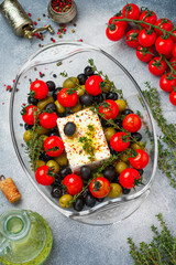 Feta cheese is ready for baking with cherry tomatoes, black and green olives, thyme, spices and garlic oil. Delicious pasta sauce. Mediterranean cuisine. Selective focus