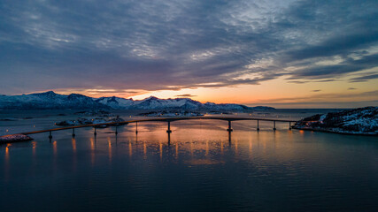 Bridge in Norway between two islands with snowy mountains and the Sunset in the background - Drone Perspective Landscape Photography