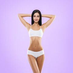 Fototapeta premium Young, fit and beautiful brunette woman in white swimsuit posing in studio. Concept of fitness, dieting and skin care.