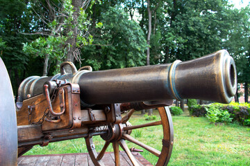 Close-up of an old bronze cannon for throwing balls against a background of green trees. Cannon on...