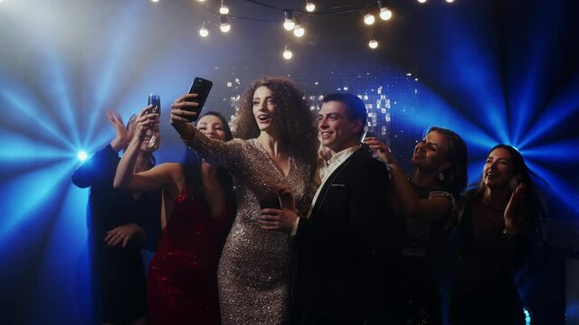 Group of happy multiethnic friends grimacing and gesturing while taking selfies and chatting via smartphone, having fun together while partying at nightclub