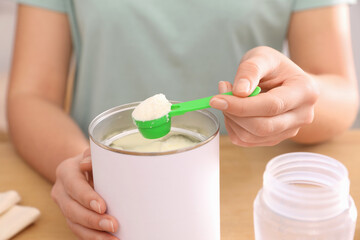 Obraz na płótnie Canvas Woman with powdered infant formula at table, closeup. Preparing baby milk