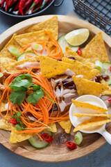 Close-up of nachos chips with shredded barbecue chicken, vegetables and dipping sauce on a wooden serving tray