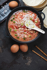 Cast-iron pan with chinese tomato egg-drop noodle soup, view from above on a brown stone background, vertical shot