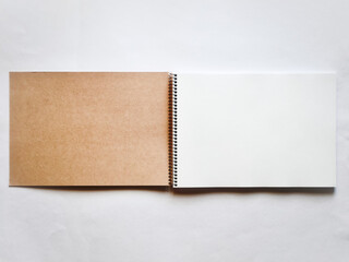 螺旋綴じの茶色いスケッチブックの見開き。茶色い表紙の裏と白い画用紙。灰色背景で真上から撮影。