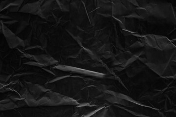 Black crumpled paper texture with folds. Black grunge surface. Black wallpaper background. 