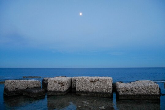 Wave breakers in harbor of Marzamemi, Sicily, at sunset with full moon.