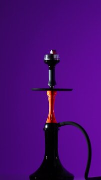 Smoking an orange hookah on a purple background with smoke. Black hookah on neon background, no people
