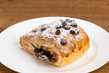 Danish Pasty filled with chocolate cream topping with chocolate chips and icing sugar in white ceramic dish on wooden table with clipping path.