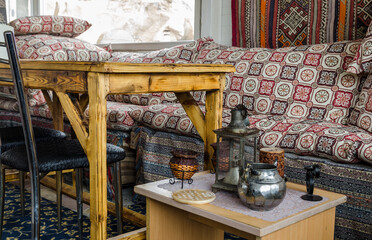 The colour woven carpet, pillows with traditional ancient patterns, lamp, kettle lying on small table, decor details inside teahouse