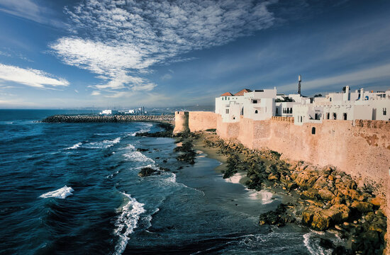 White Painted Historical Buildings And City Wall Of Asilah Against Blue Sky At Coast, Morocco, North Africa