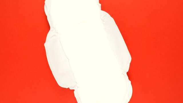 Menstrual sanitary pad is slowly rotating on red background.