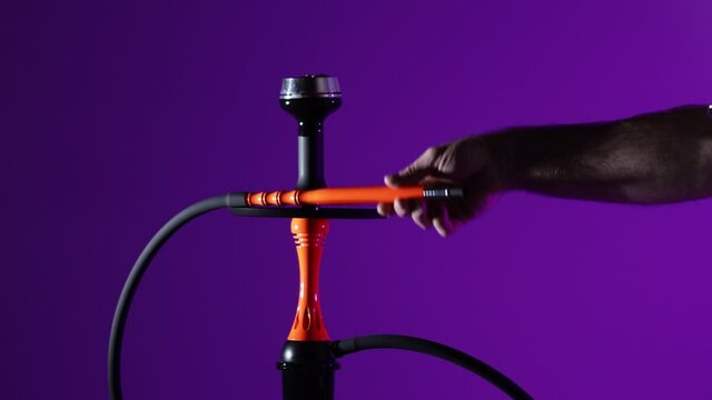 Smoking an orange hookah on a purple background with smoke. Black hookah on neon background, no people
