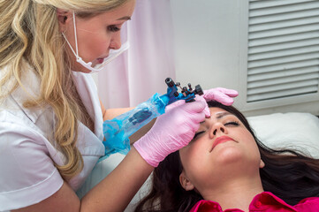 Young woman doing eyebrow microblading in a beauty salon 