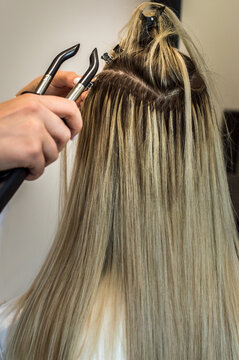 Hair extension process of a young woman in a beauty salon close-up.