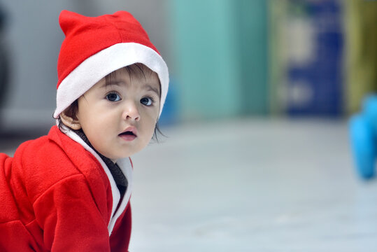 Indian baby girl wearing Santa Claus dress on Christmas Day crawling on the floor