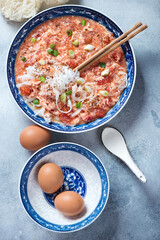 Plate of chinese tomato egg-drop noodle soup, flatlay on a light-blue stone background, vertical shot