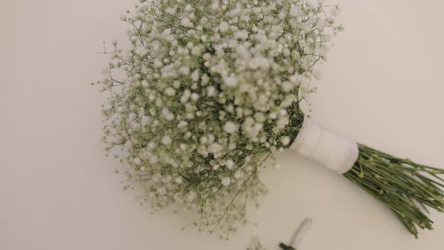 Two wedding bouquets of white gypsophila flowers lie down on white background. Bouquets of bride and groom. Morning preparations of newlyweds. Floral arrangement in bedroom. Slow motion, indoors
