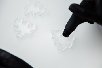 A transparent lollipop in the form of a Christmas tree lies on a white surface and is burned with a lighter. High quality photo