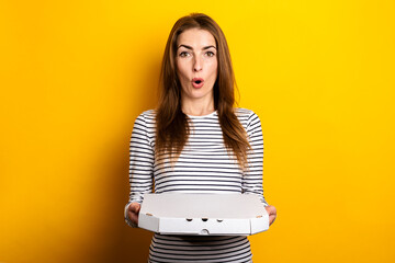 surprised shocked young woman holding packaged pizza on yellow background