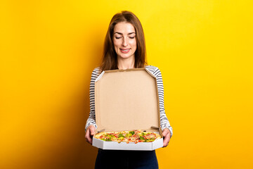 smiling young woman holding package with hot fresh pizza on yellow background