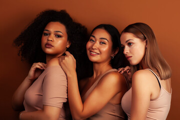 young pretty asian, caucasian, african woman posing cheerful together on brown background, lifestyle diverse nationality people concept