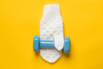 Dumbbell on a white, knitted mitten, on a yellow background. Healthy and active lifestyle concept. Top view. 