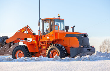 Big orange tractor cleans up snow from the road and loads it into the truck. Cleaning and cleaning...