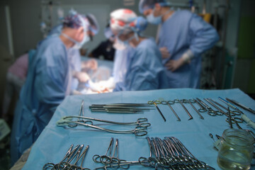 Closeup of surgical tools on table and team of surgery doctors operating a patient in hospital room