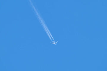 Distant passenger jet plane flying on high altitude on clear blue sky leaving white smoke trace of contrail behind. Air transportation concept
