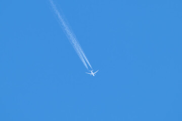 Distant passenger jet plane flying on high altitude on clear blue sky leaving white smoke trace of...