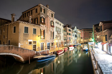 Fototapeta na wymiar Night scene of illuminated old buildings, floating boats and reflections in canal water in Venice, Italy.