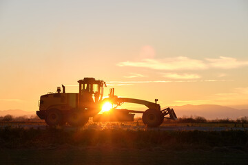Fototapeta premium Silhouette of heavy duty tractor driving on road at sunset