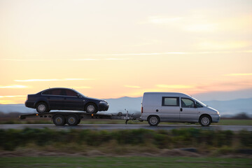 Obraz premium Tow truck vehicle with car transporting carrier trailer driving on highway in evening