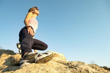 Woman hiker climbing steep big rock on a sunny day. Young female climber overcomes difficult climbing route. Active recreation in nature concept.