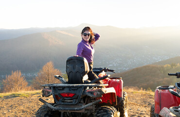 Young happy female driver enjoying extreme ride on ATV quad motorbike in fall mountains at sunset. © bilanol