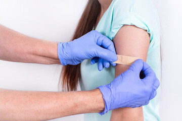 Doctor or nurse glues bandage on patient's shoulder after an injection or vaccination. Close-up....