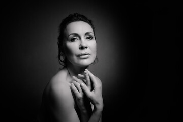 Portrait of a sensual fifty year old woman on grey studio background. Monochrome shot.