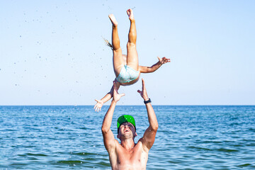 Young man dad tosses the baby girl up on the beach.