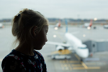 child at the airport looks at the plane outside the window. Airline travel concept.