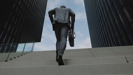 Back view of businessman walking on stairs in hurry - Powered by Adobe