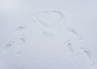 Traces, prints of bare feet in the snow lead to the painted heart. Background for Valentine's Day cards.